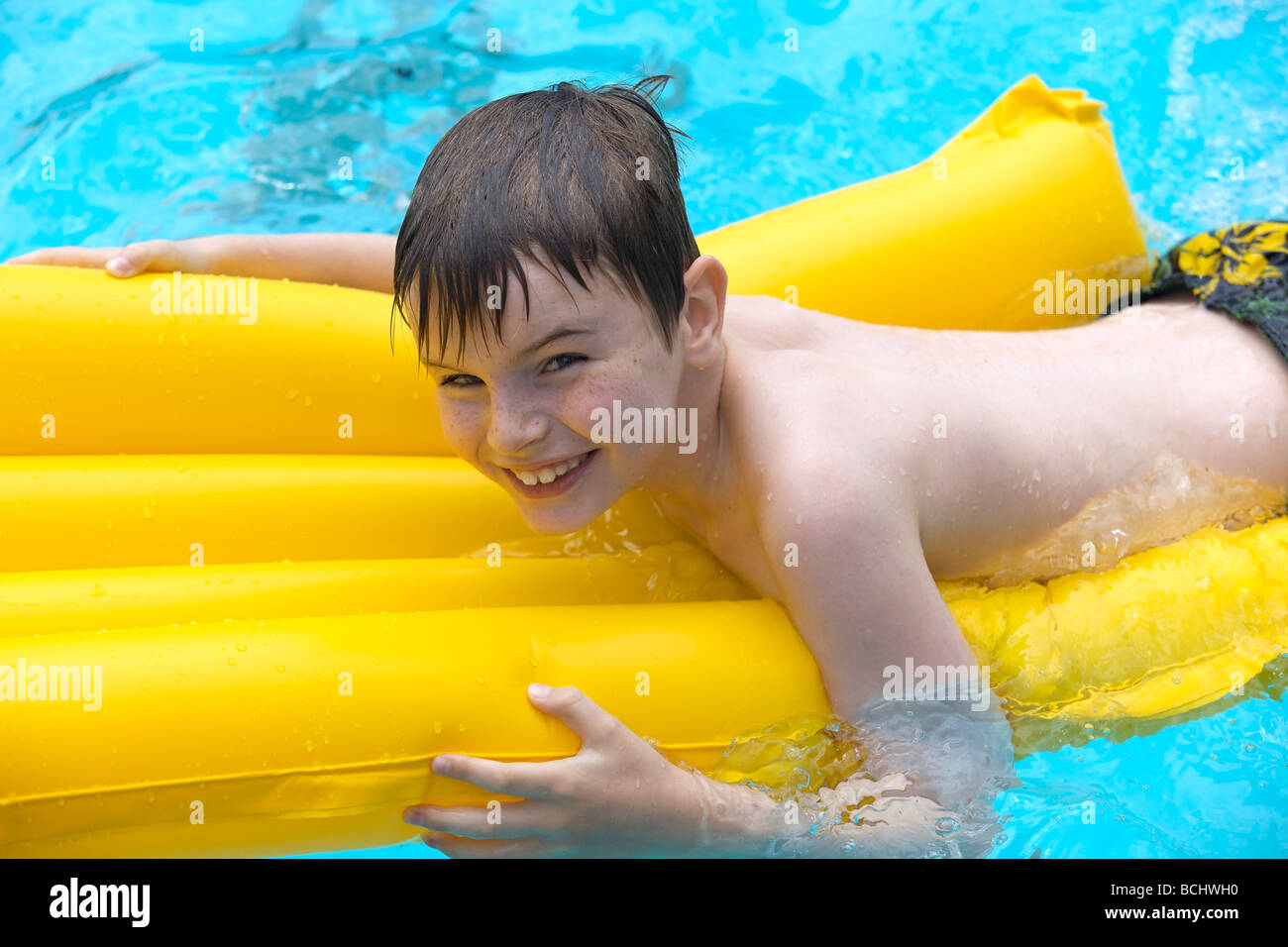 Happy young boy relaxing at the swimming pool on a yellow lilo Stock
