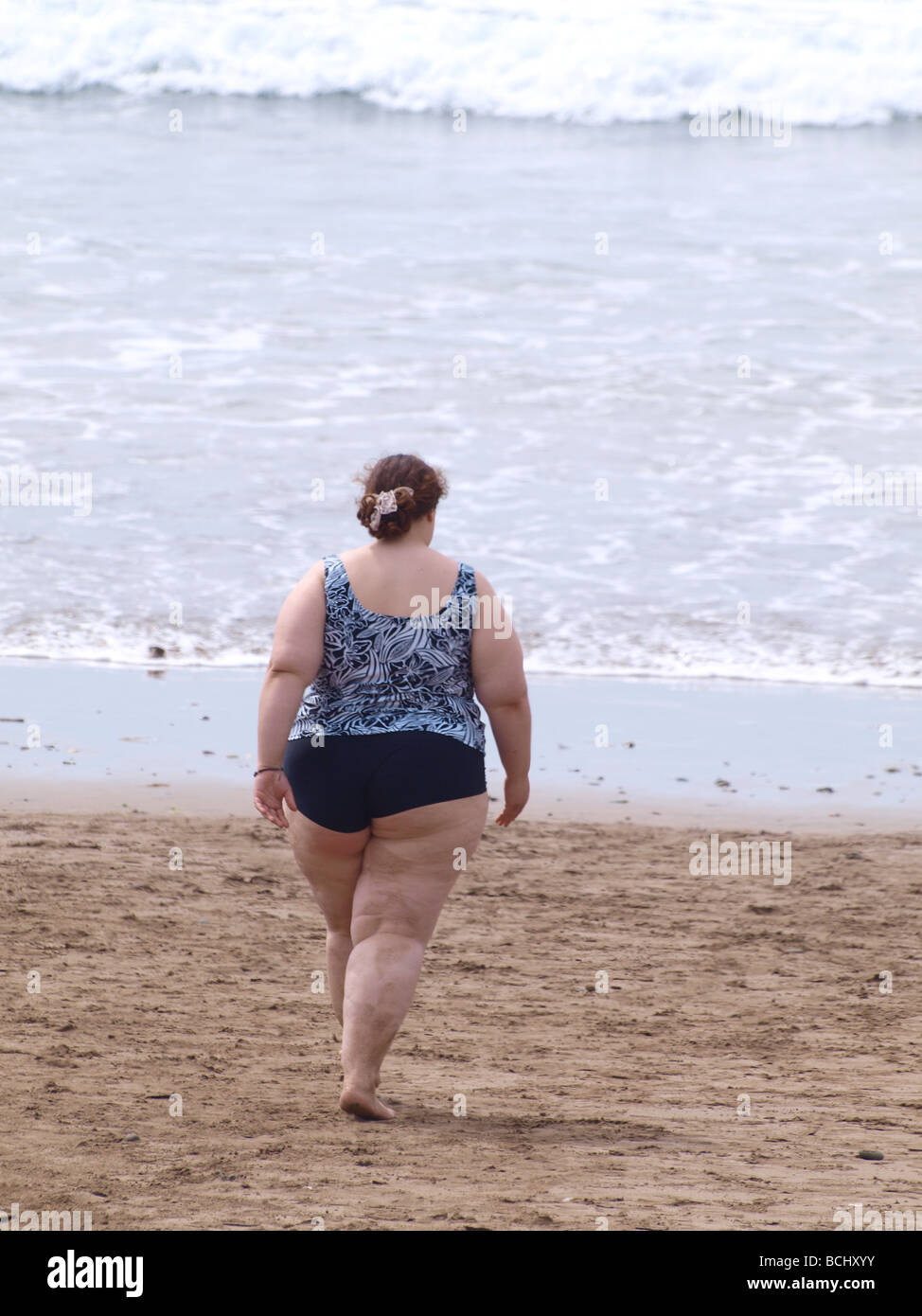 Very obese woman walking towards the sea Stock Photo