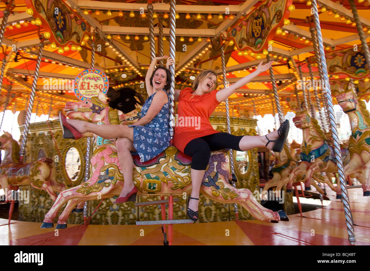 Two girls on a day out in Brighton riding on the carousel on the beach. Stock Photo