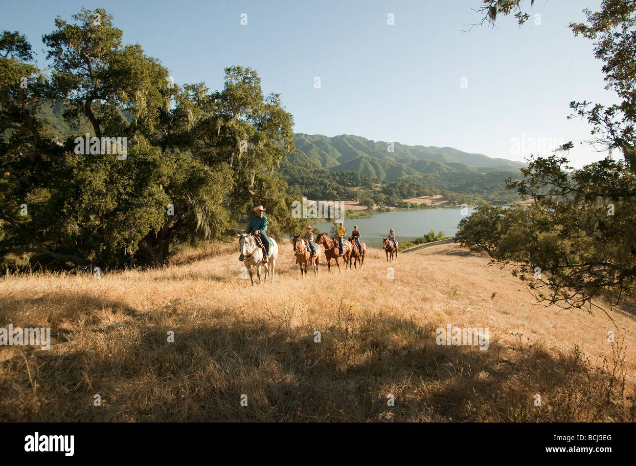 Horse riders on hill covered with grass and oak trees overlooking Lake Alisal at Alisal Ranch in Solvang, California, USA. Stock Photo