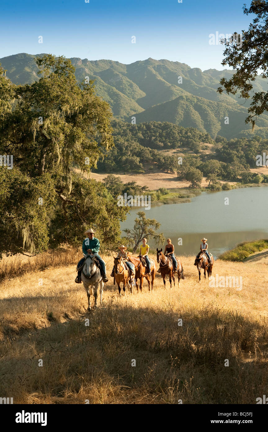 Horse riders on hill covered with grass and oak trees overlooking Lake Alisal at Alisal Ranch in Solvang, California, USA. Stock Photo