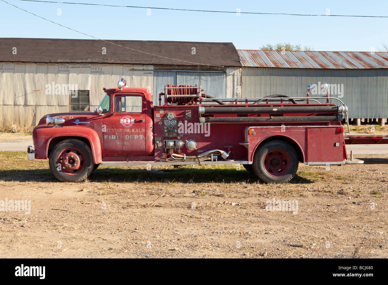 Fire truck fire engine parked in field with metal corrugated buildings in background Profile view De Kalb Texas USA Stock Photo