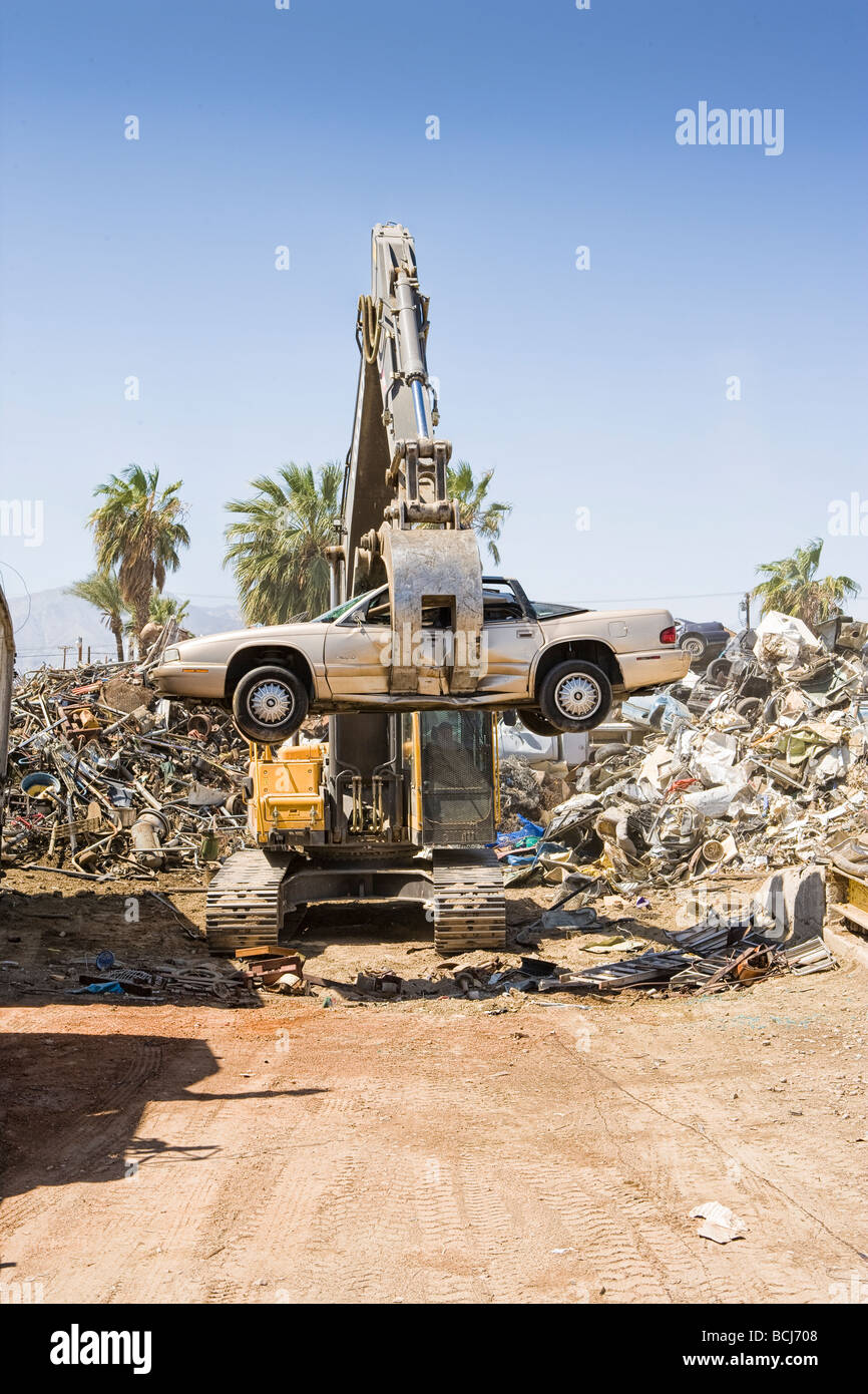 Machine crane holding crushed automobile car at metal recycling center Indio California USA Stock Photo