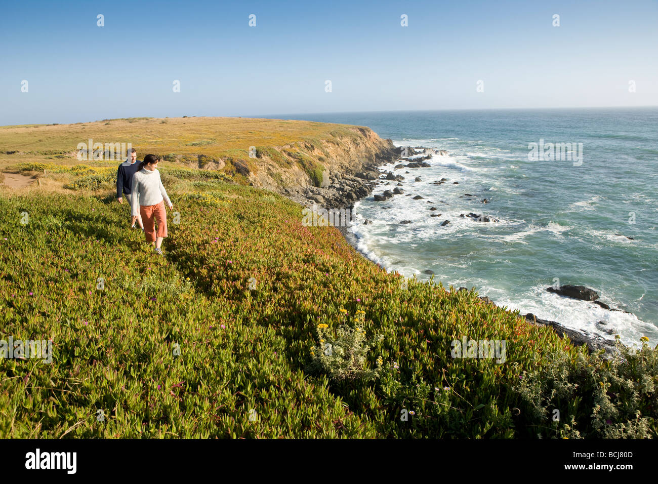 Male and female couple walking on path along cliffs beach in Cambria California with view of ocean Stock Photo