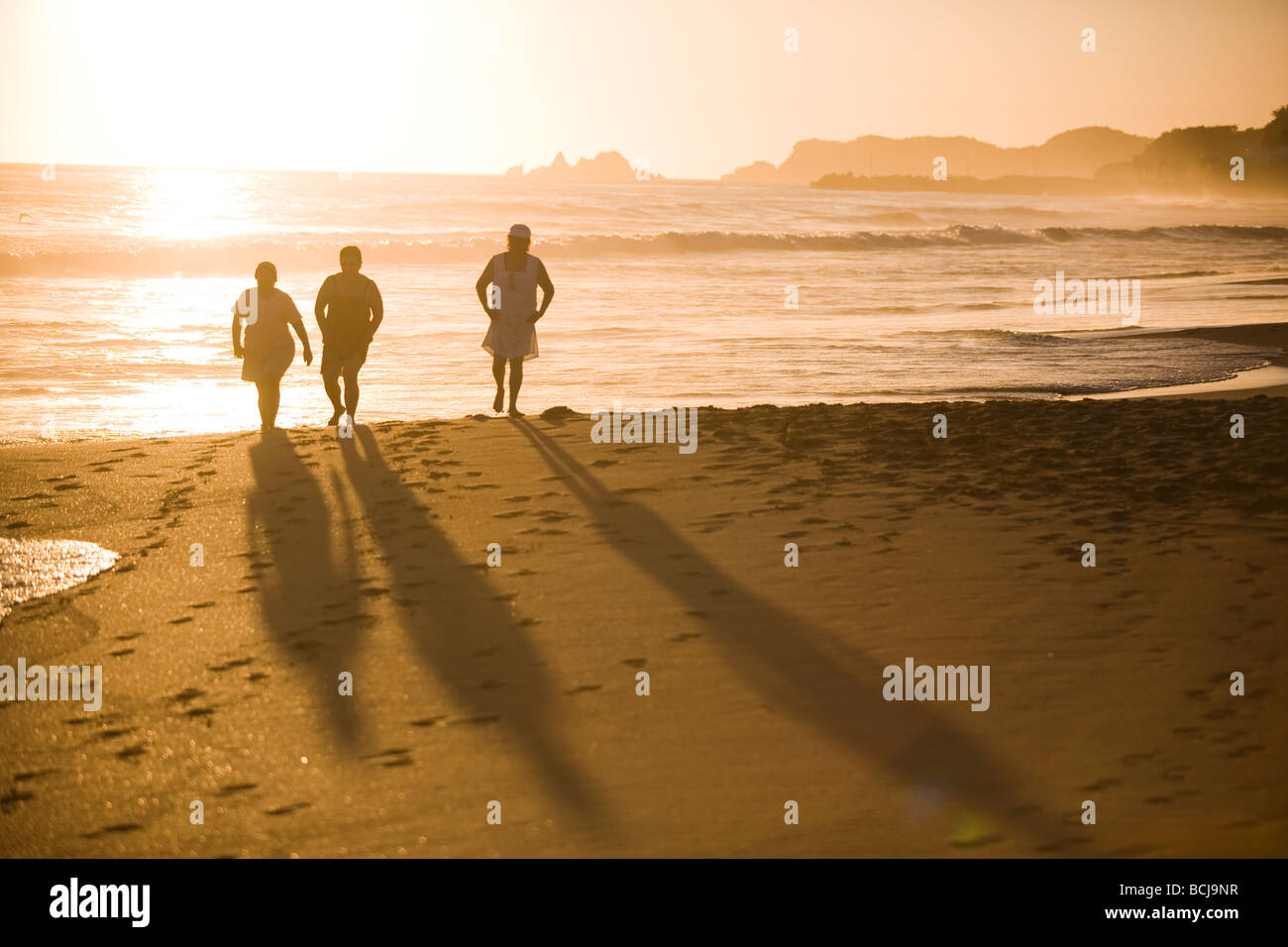Ixtapa Mexico Three persons in in silhouette walking on beach, sun setting on Pacific Ocean behind them. Stock Photo