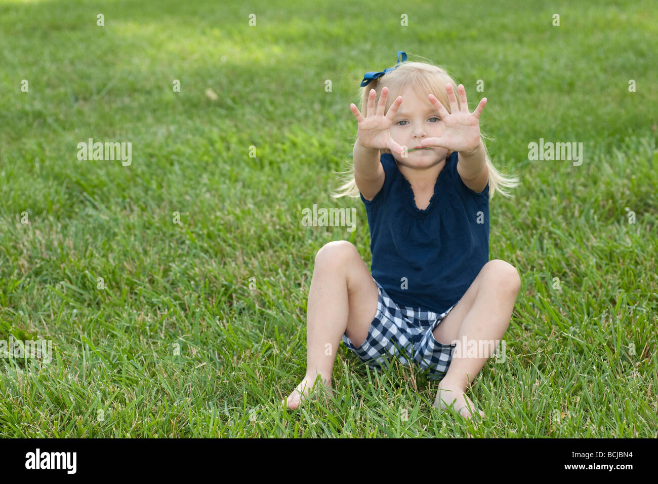 Little girl sitting in the grass showing expression Stock Photo - Alamy