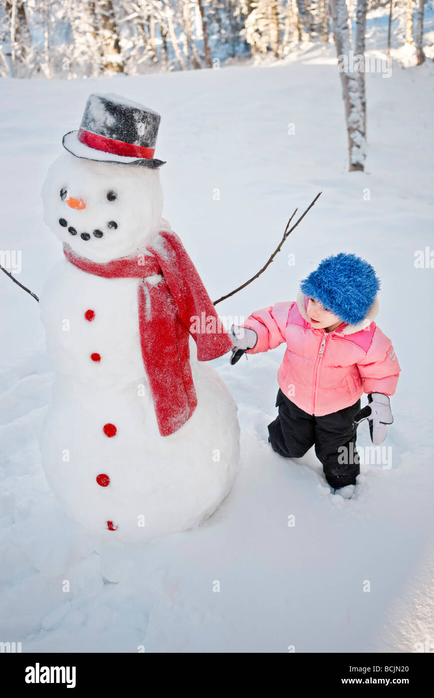 Young girl decorates a snowman with red scarf and black top hat, Alaska Stock Photo