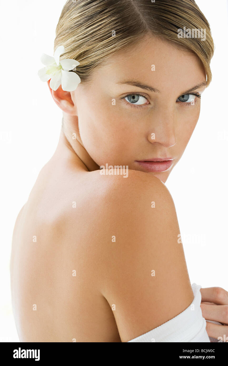 Portrait of young woman with bare shoulders and a frangipani in her ...