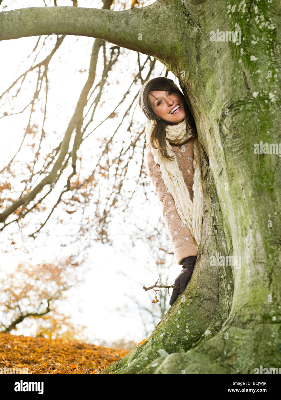 Smiling woman standing behind a tree Stock Photo
