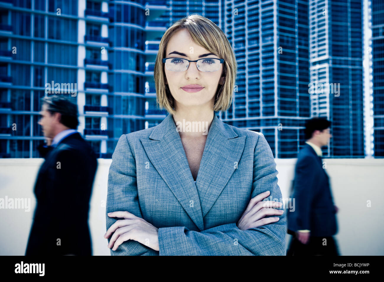Young pretty businesswoman staring into camera with motion blurred businessmen walking by Stock Photo