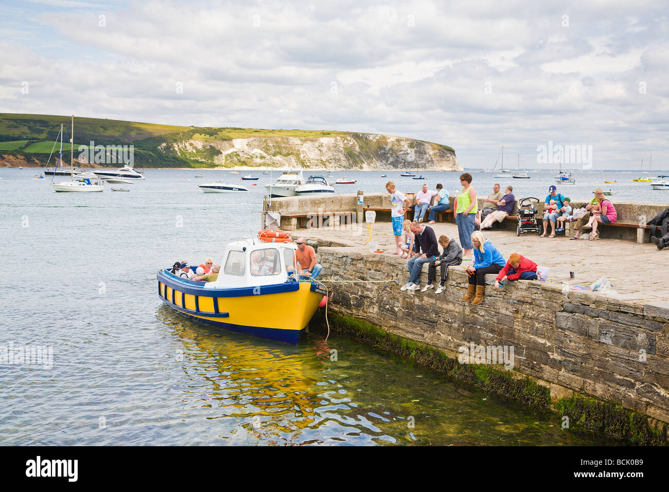 Families crabbing off the harbour wall and a boat for pleasure trips around the bay.  Seaside town of Swanage, Dorset. UK Stock Photo