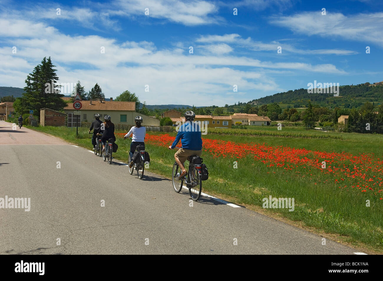 A party of cyclists on electric bicycles are touring the quiet poppy lined country roads of Provence France Stock Photo