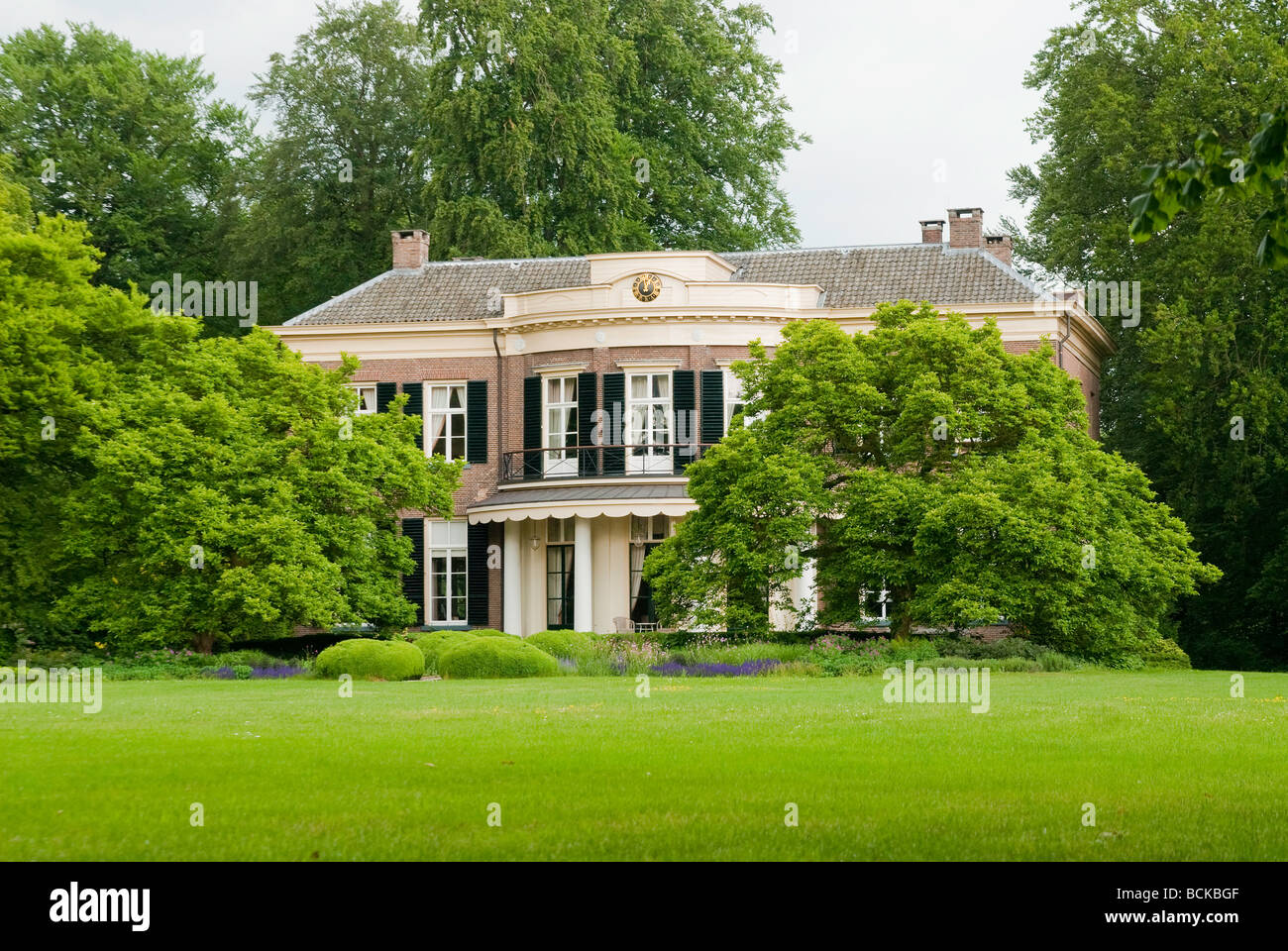 Mansion 't Enzerinck in Vorden, Netherlands, partially covered by lush green trees and a lush green lawn in front Stock Photo