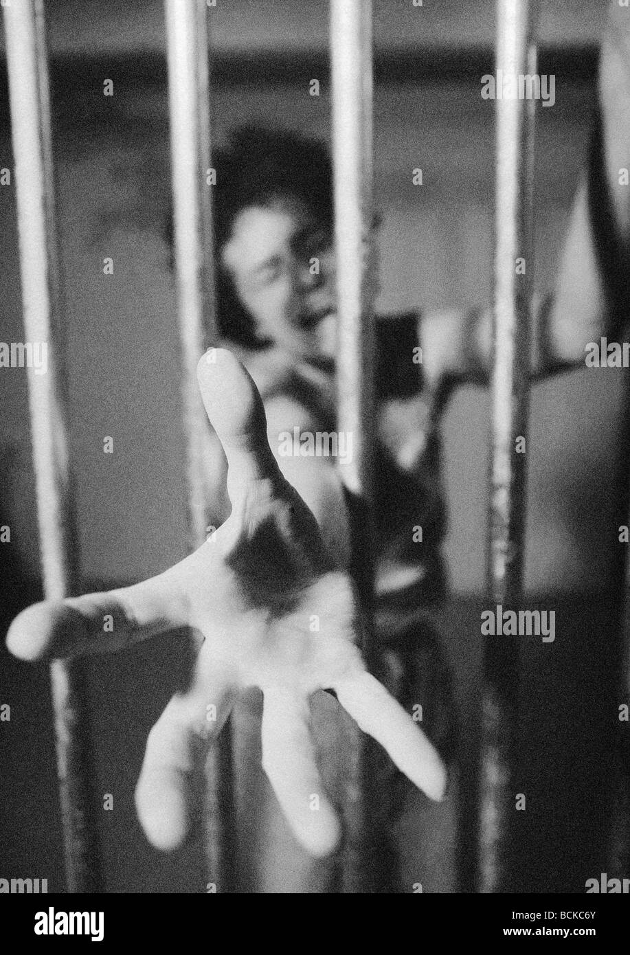 Woman behind prison bars reaching hand through bars, b&w Stock Photo