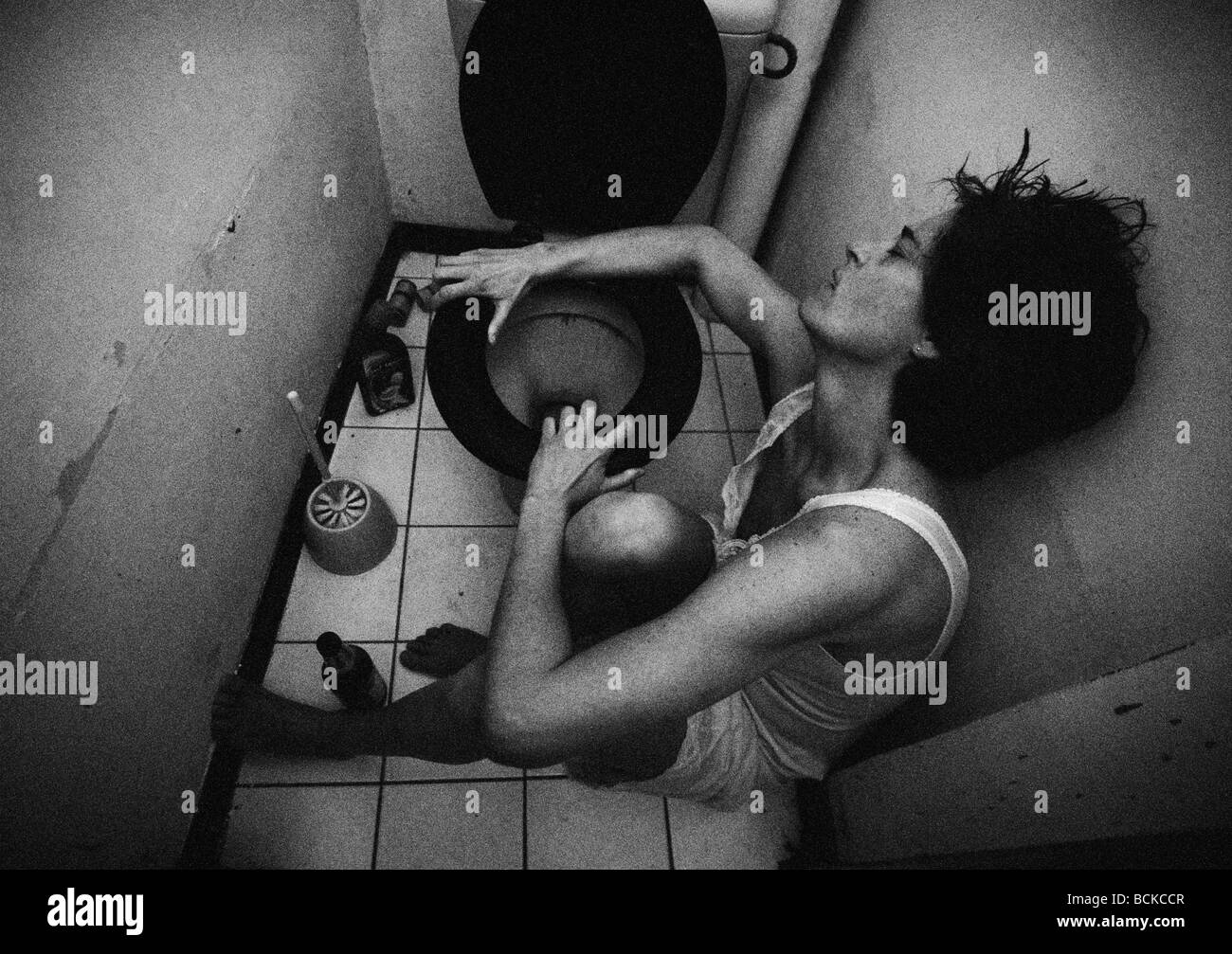 Woman sitting on bathroom floor holding onto toilet, b&w Stock Photo