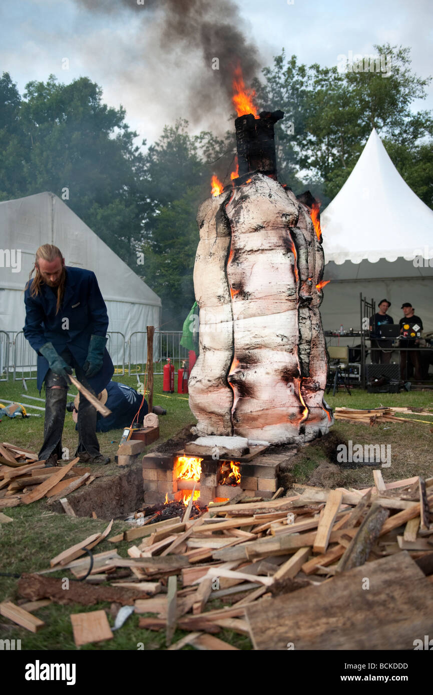 Man Stoking the outdoor kiln enveloping TOM s ceramic fire