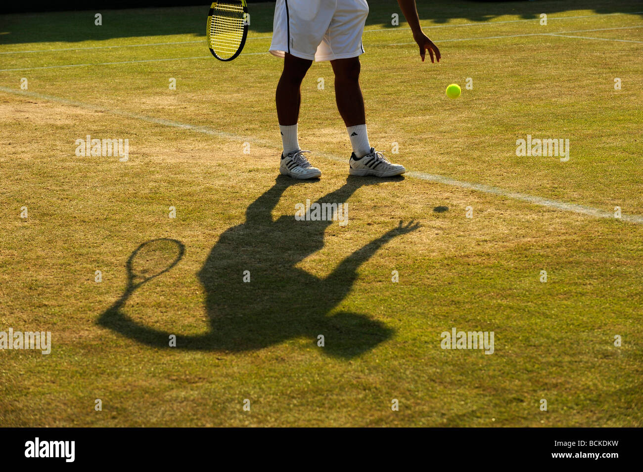 A player and shadow as he bounces the ball before serving during the