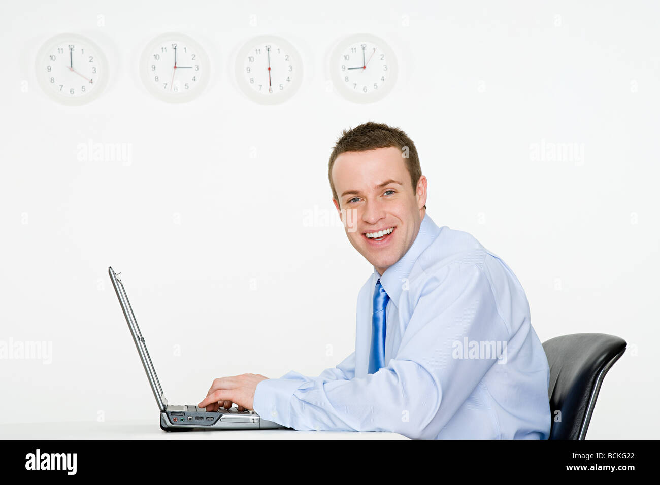 Office worker with laptop and wall clocks Stock Photo