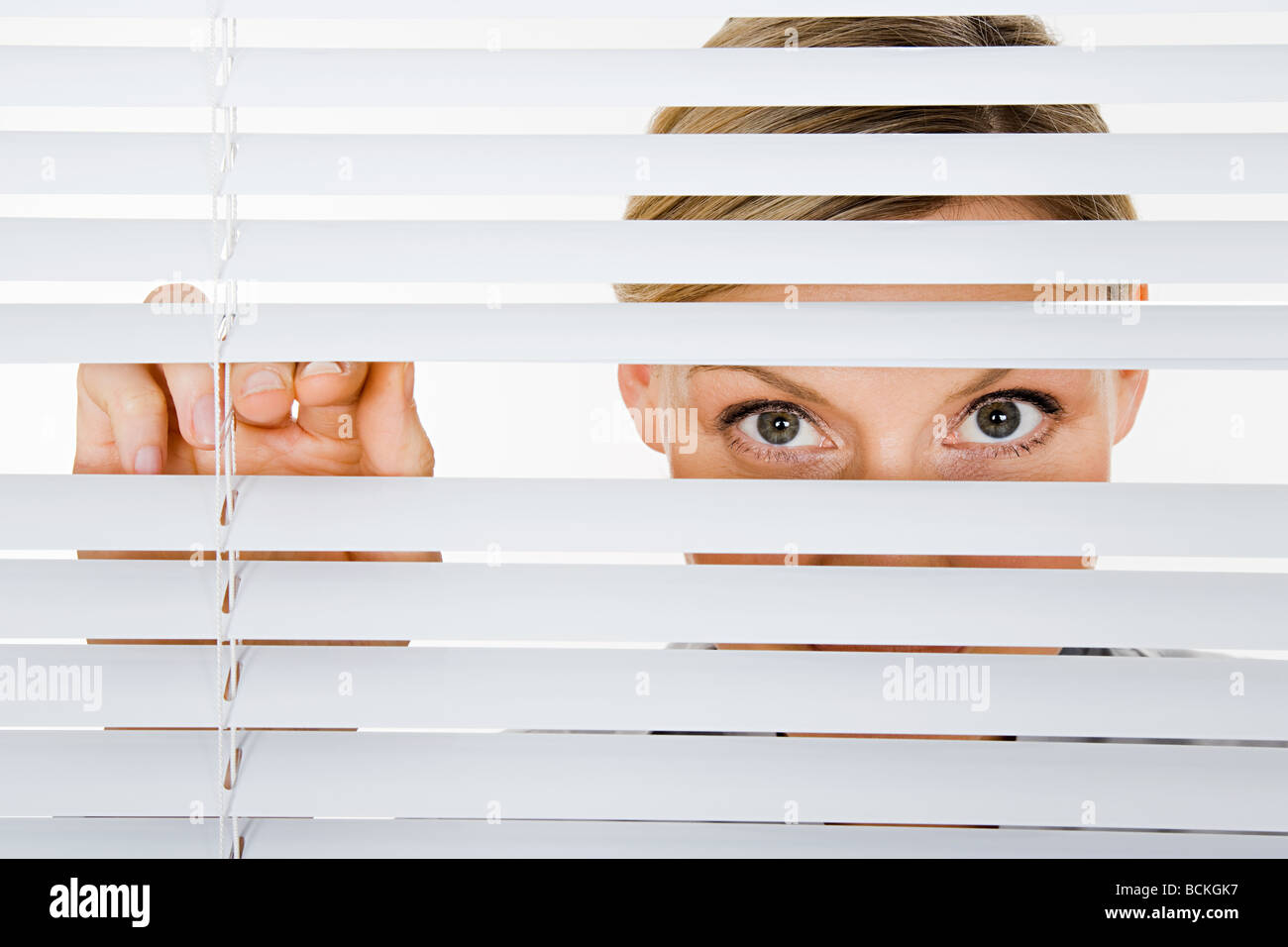 Woman looking through blinds Stock Photo