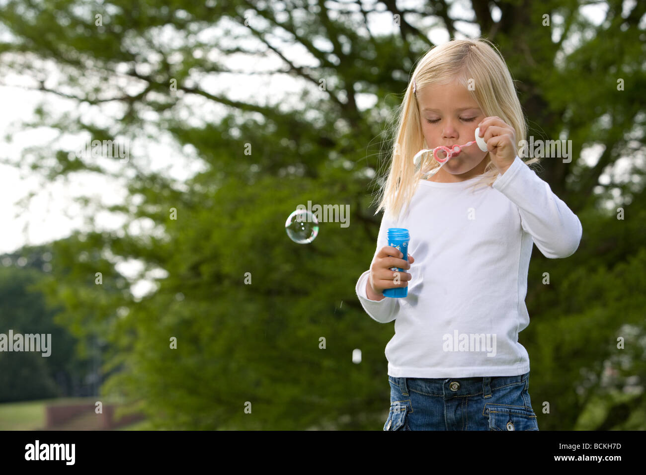 Adorable young girl blowing soap bubbles in the park Stock Photo - Alamy