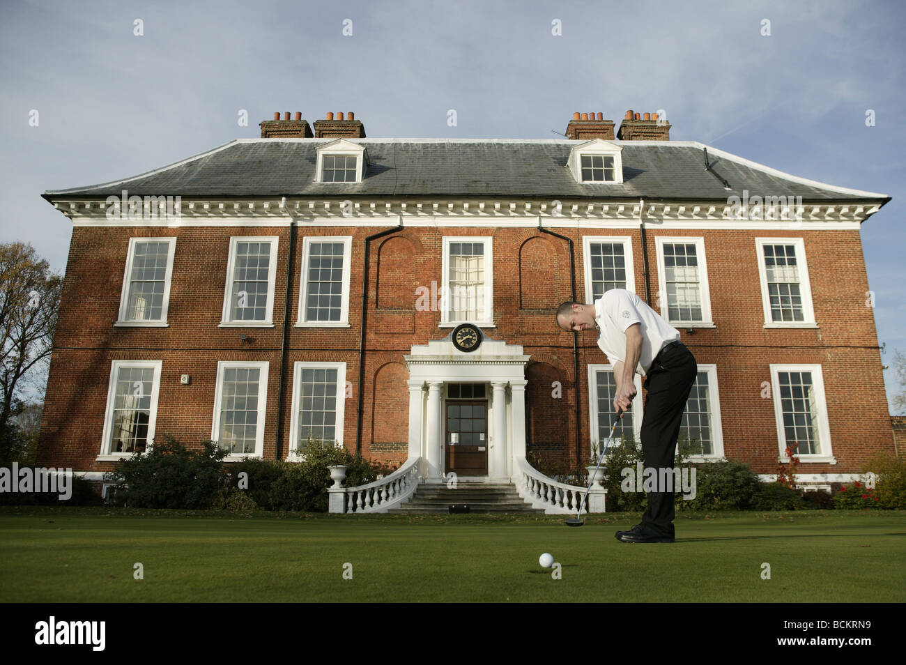 A Golfer takes a putt in front of a prestigious Club House. Stock Photo