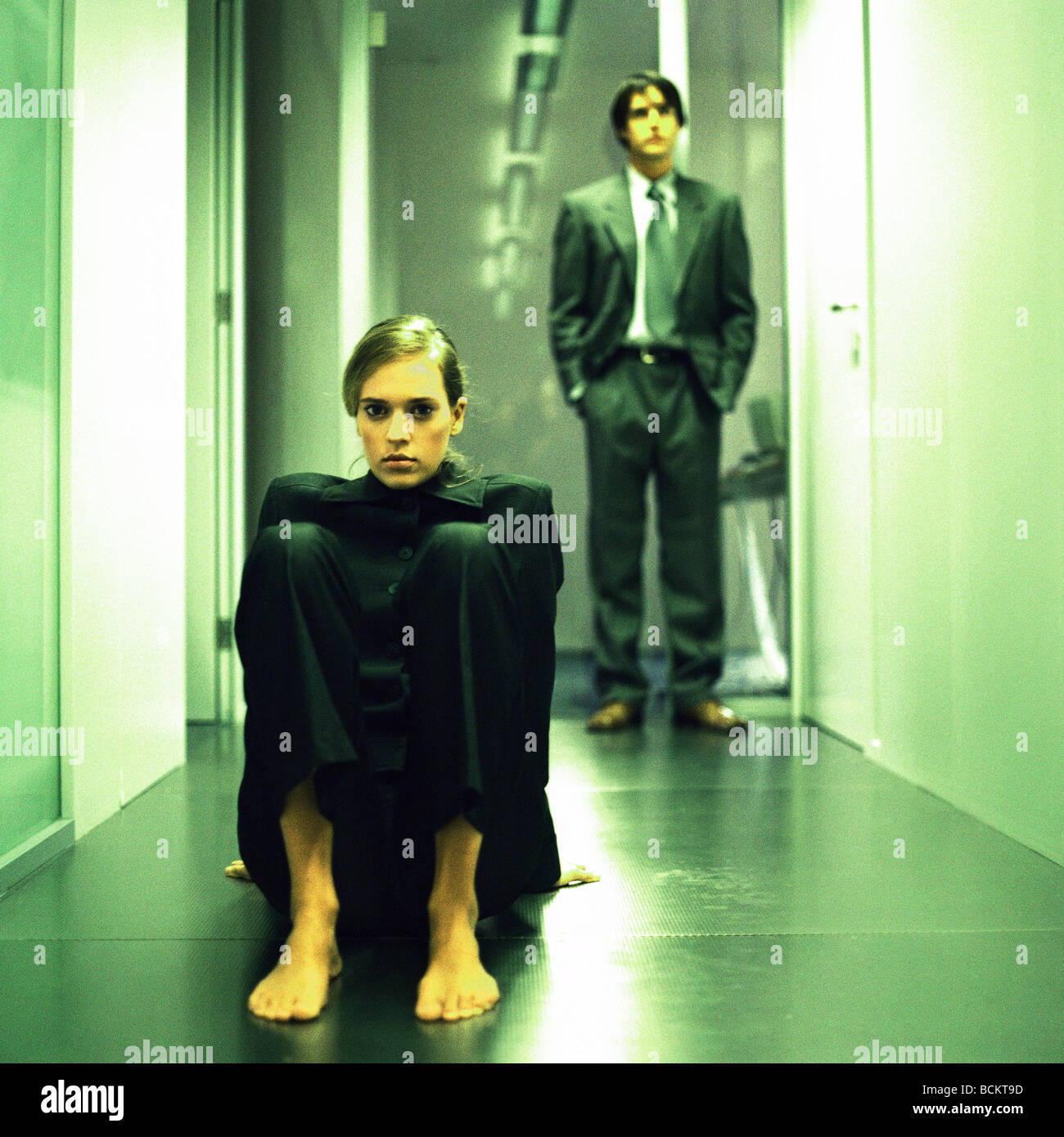 Woman sitting on floor in hallway, man standing behind Stock Photo