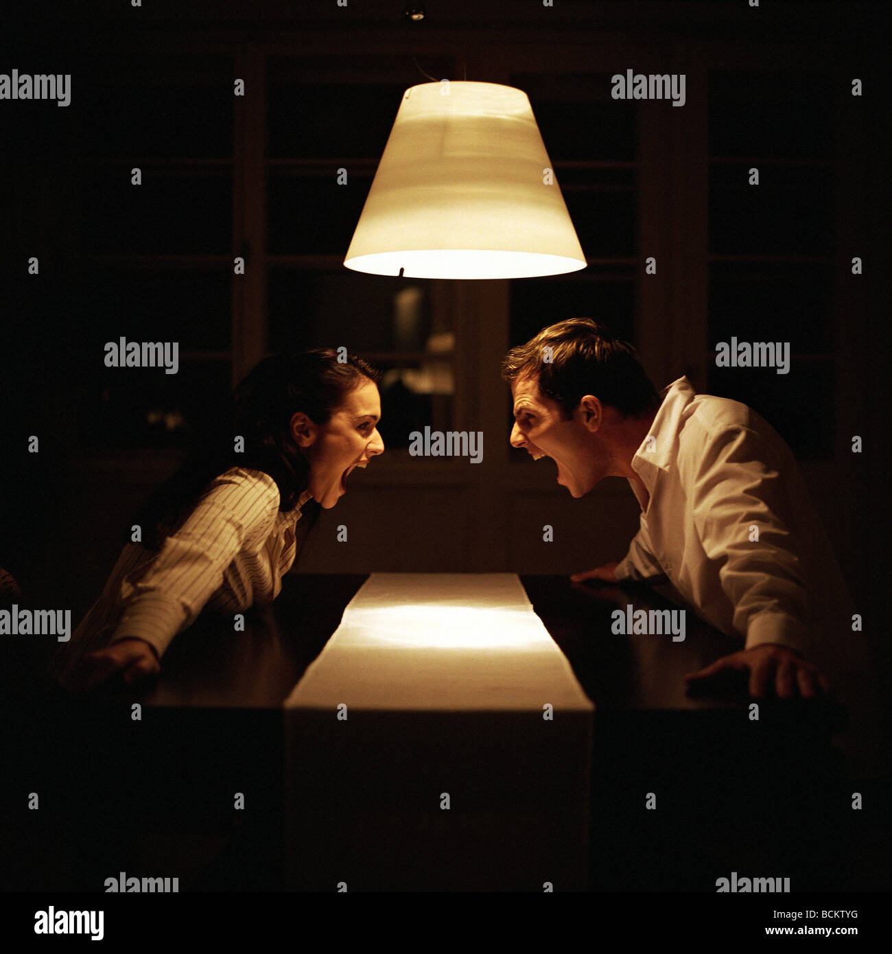 Man and woman face to face at table, screaming at each other Stock Photo