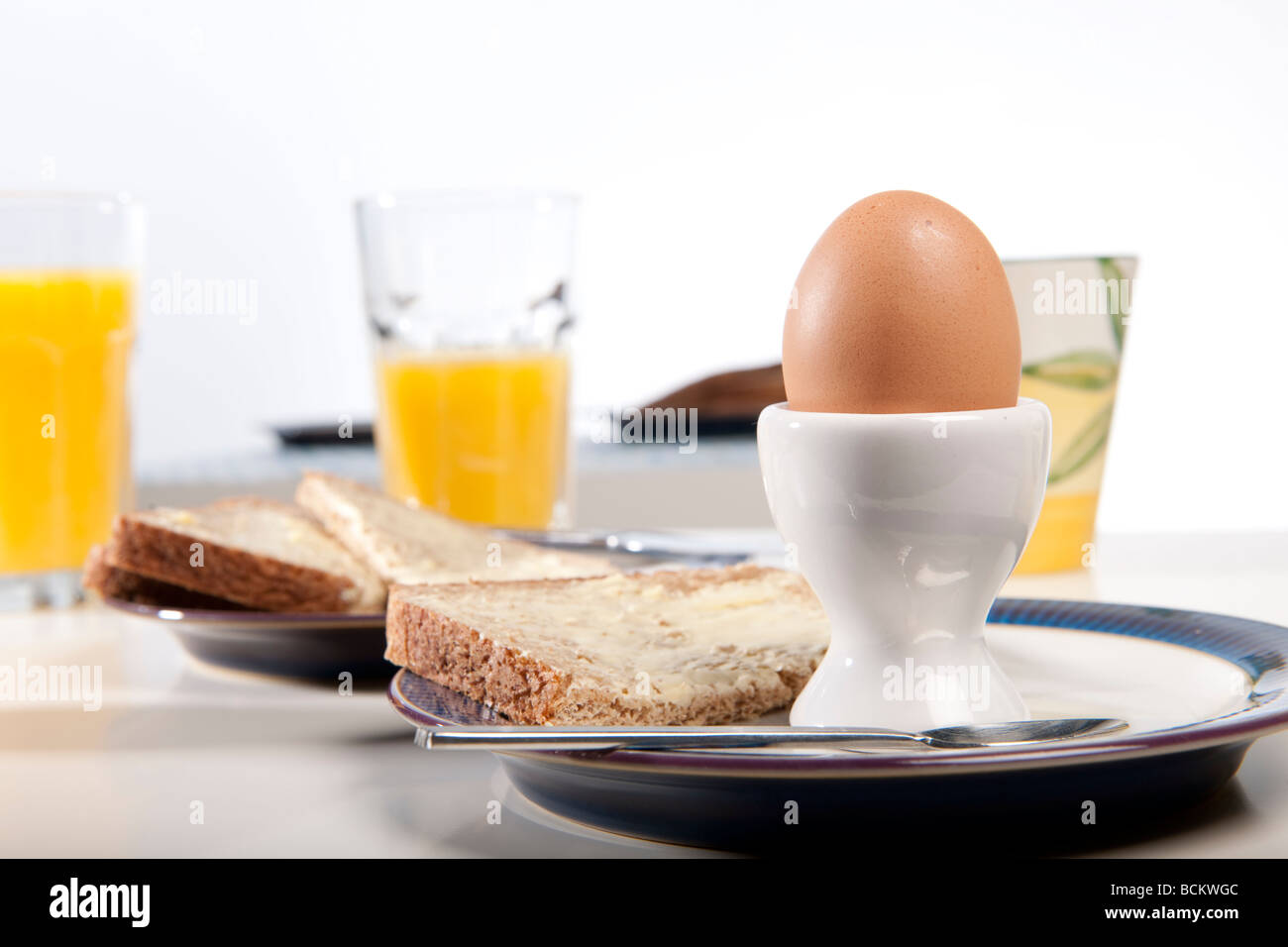 Breakfast scene, containing eggs, orange juice, bread, butter, cups