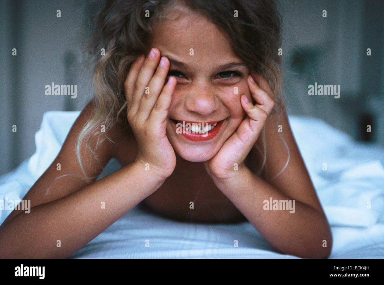 Girl lying in bed, leaning on elbow and laughing Stock Photo