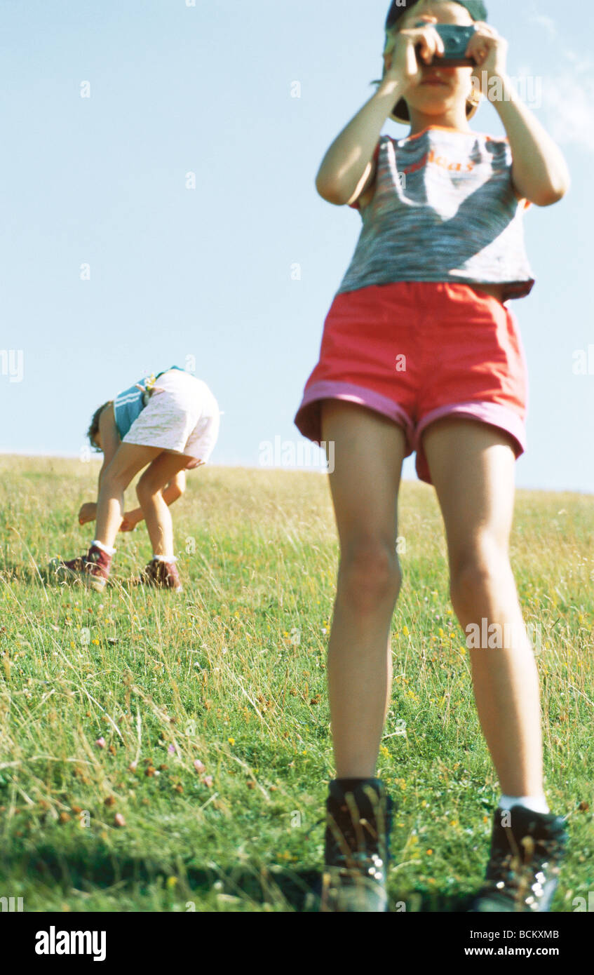Girl Taking Photo Second Child Bending Over Looking At Grass In Background Girl Taking Photo Second Child Bending Over Looking At Grass In Background