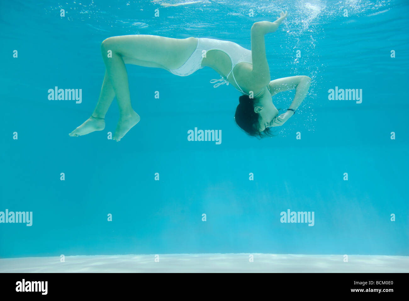 Teen girl underwater in swimming pool, holding nose, side view, full length Stock Photo