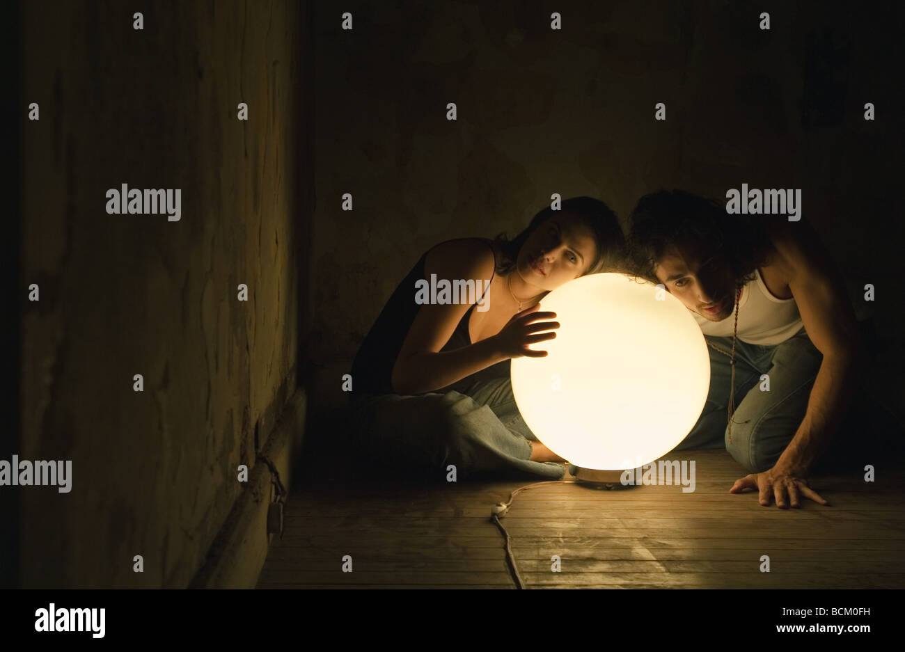 Woman and man putting ears to glowing orb Stock Photo