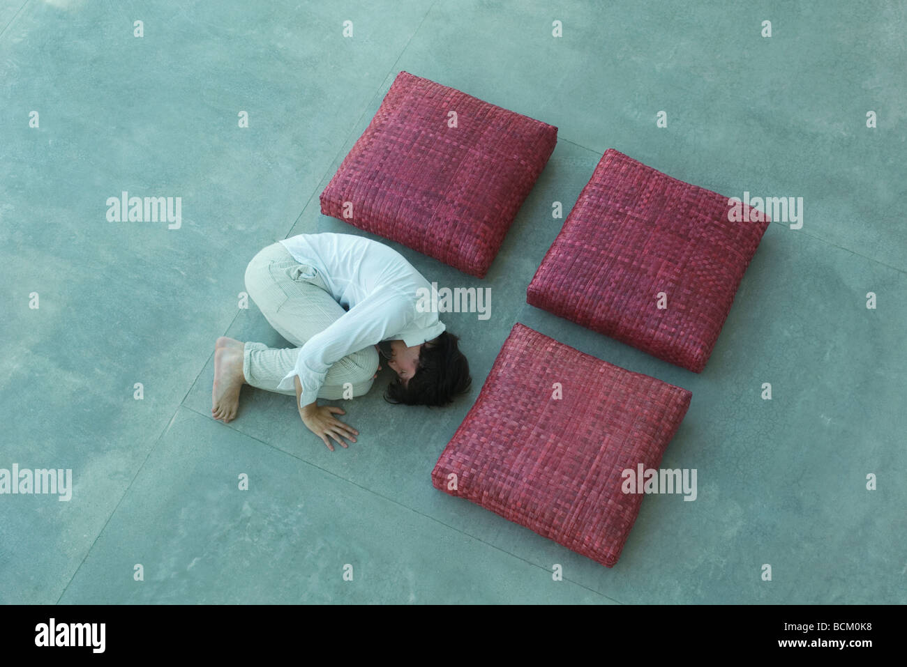Three square cushions and man arranged in square shape, man lying in fetal position, high angle view Stock Photo