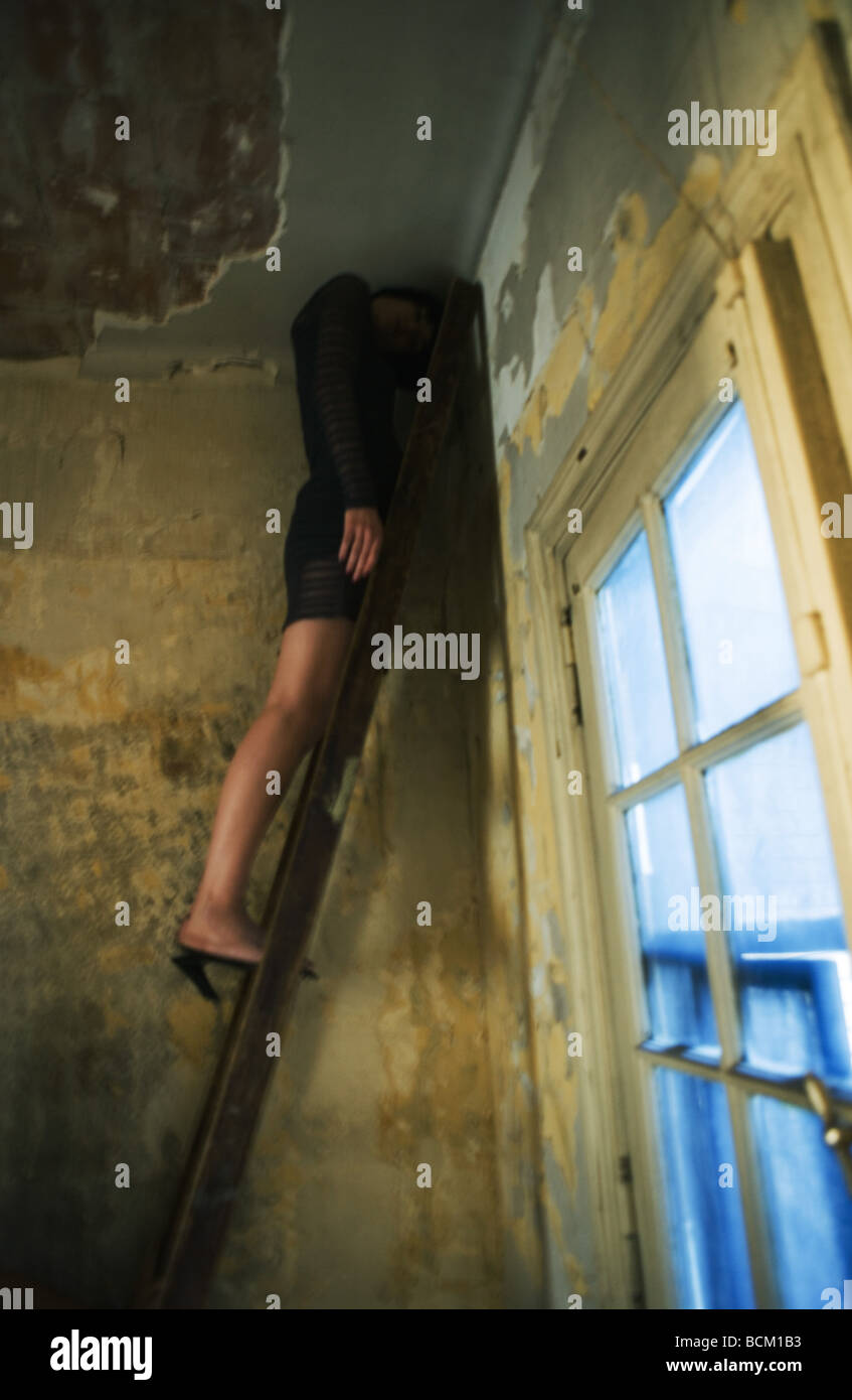 Woman standing on ladder in corner of room, head bent down under ceiling, full length, low angle view Stock Photo