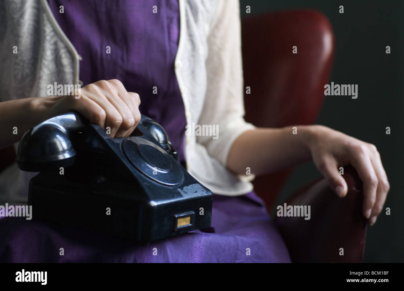 Woman in dress sitting with telephone on lap, hand on receiver, cropped view of mid section Stock Photo