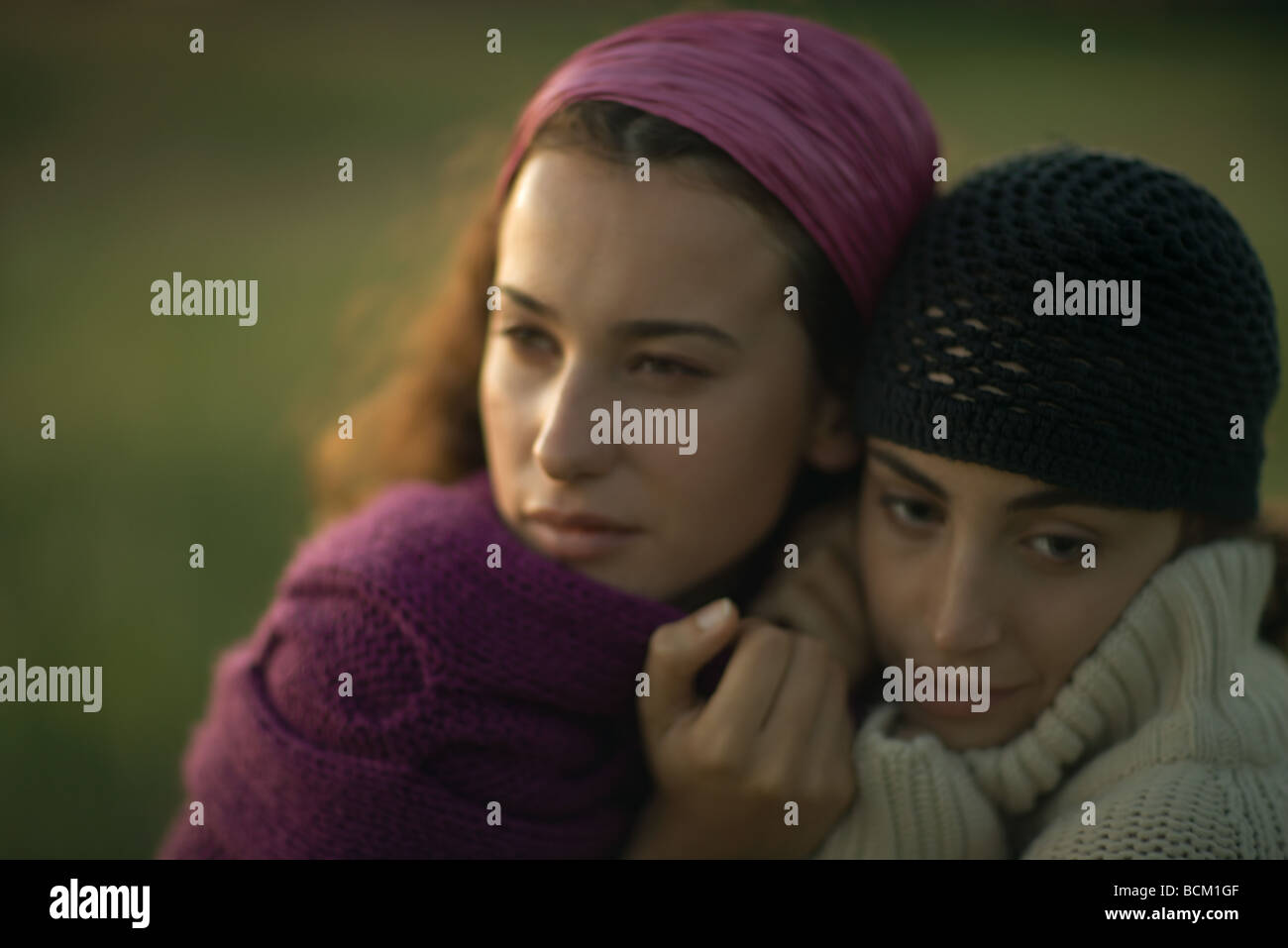 Two women huddling together, pulling sweaters up to faces, looking away, close-up Stock Photo