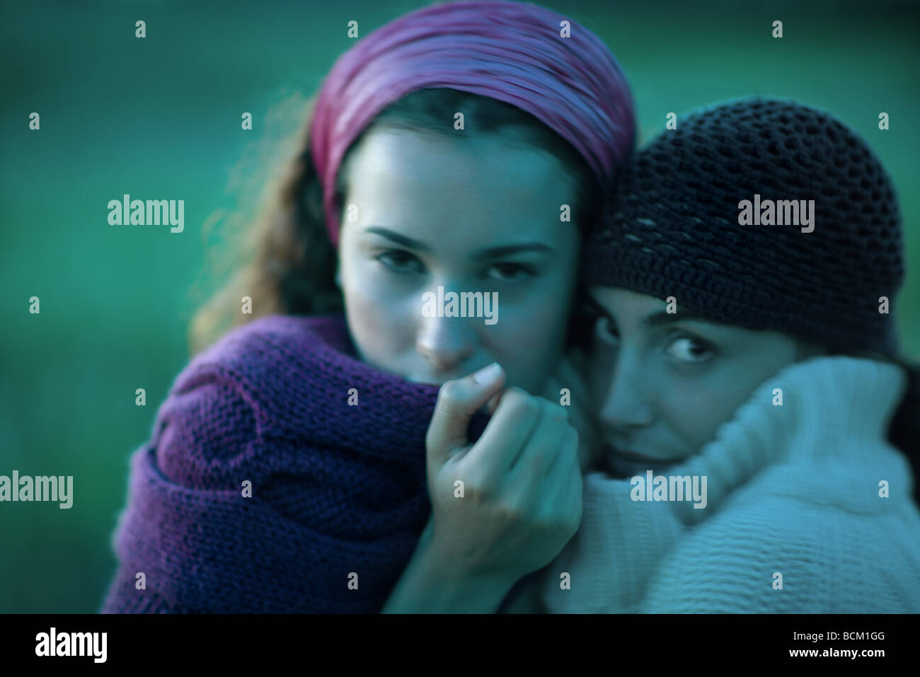 Two women huddling together, pulling sweaters up to faces, looking at camera, close-up Stock Photo
