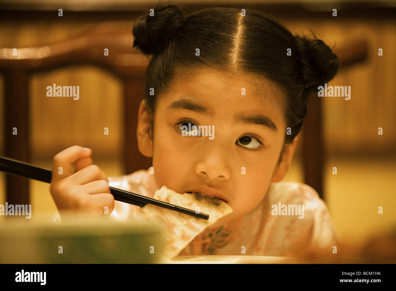 Girl eating with chopsticks, looking up, head and shoulders Stock Photo