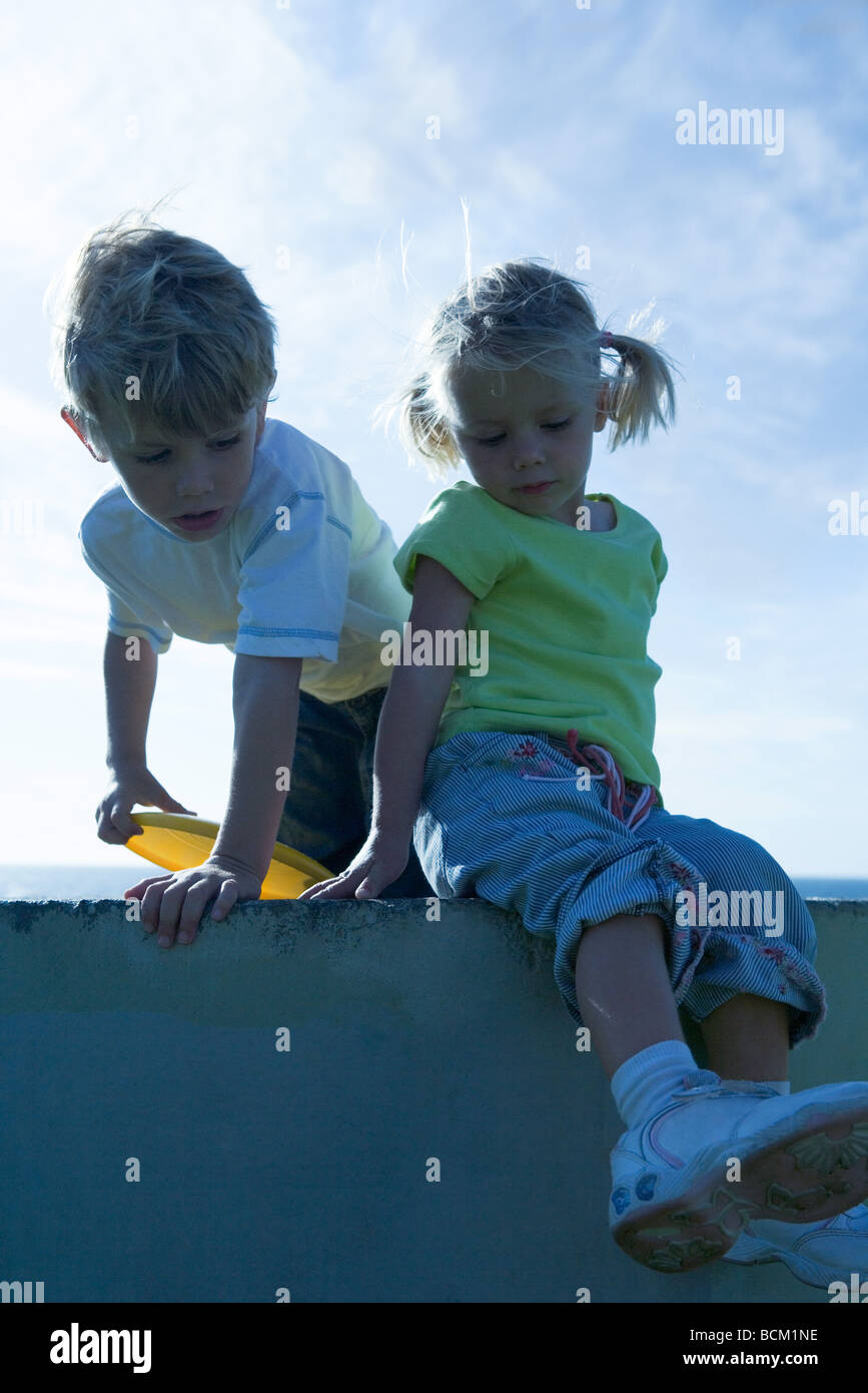 Boy and girl on wall, sky in background Stock Photo