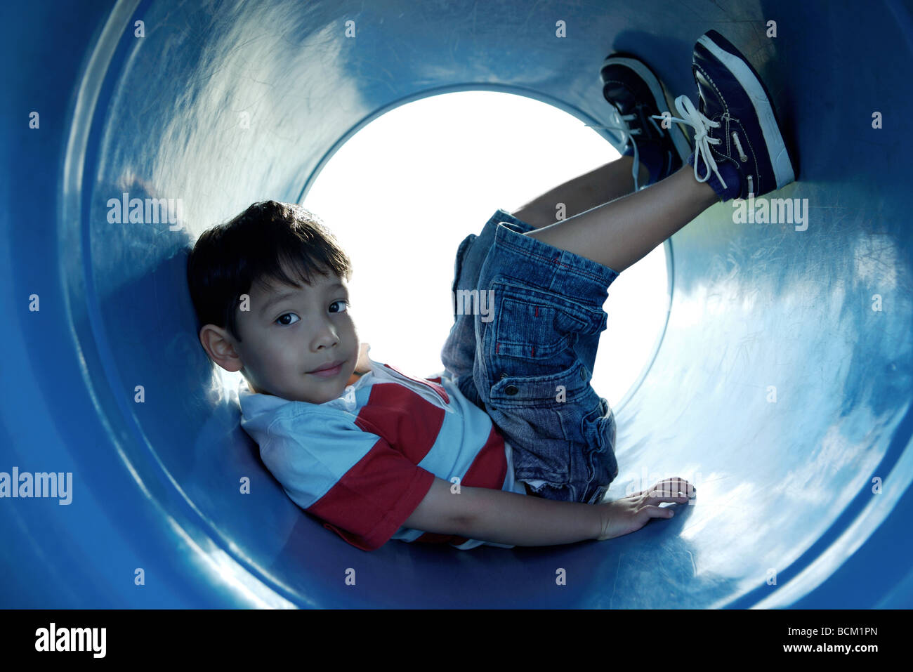Boy sitting in playground tunnel with legs up, looking at camera, full length Stock Photo Alamy