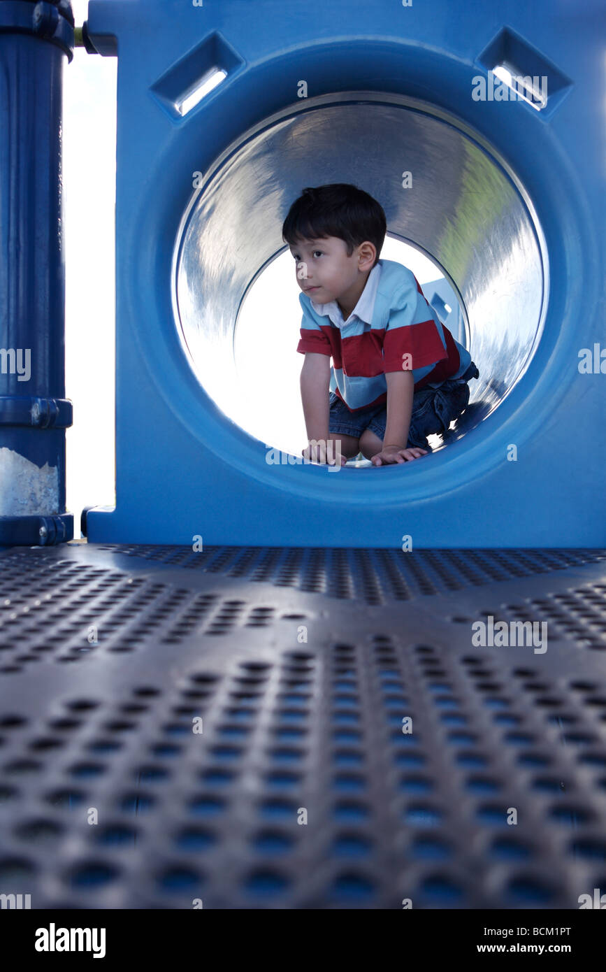 Boy crouching in playground tunnel, full length Stock Photo