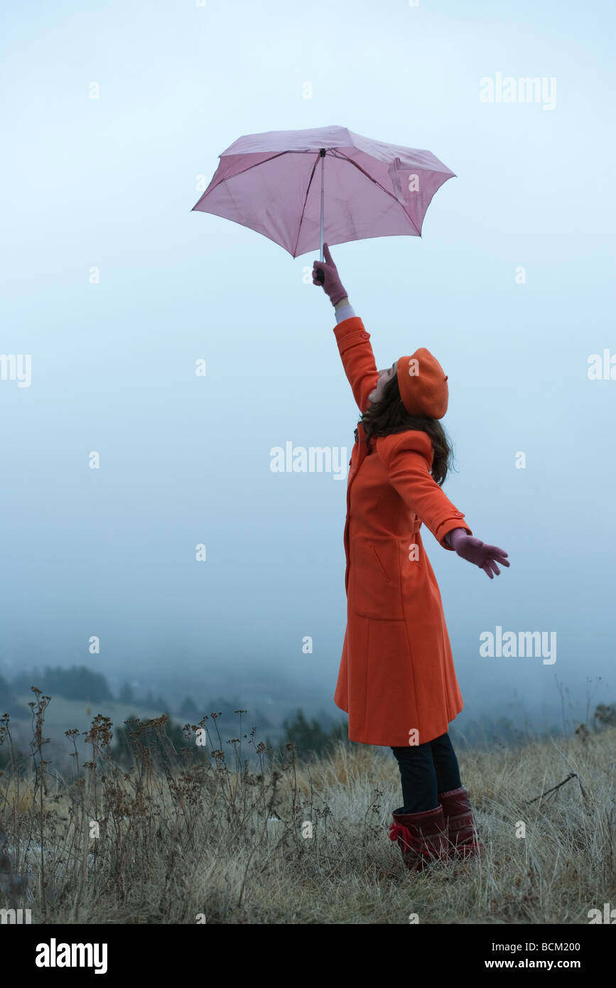 Teenage girl standing outdoors, holding up umbrella, side view Stock