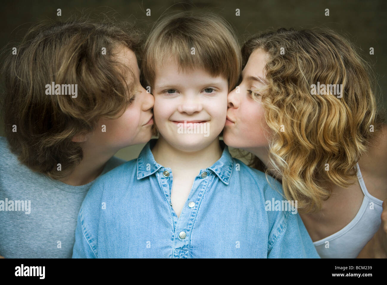 Girl with Down's Syndrome smiling at camera as two sisters kiss her cheeks, portrait Stock Photo