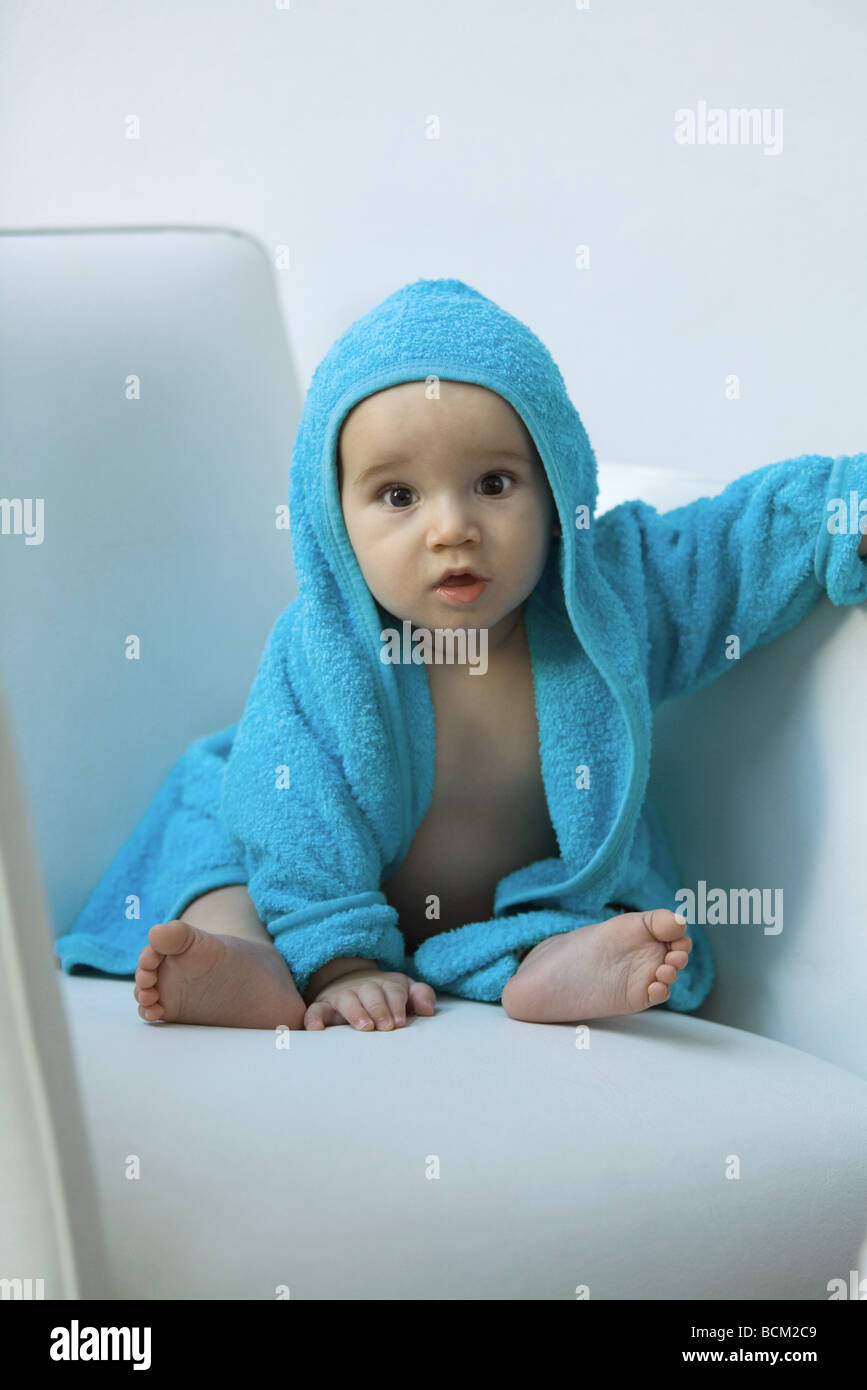 Baby wearing hooded bathrobe sitting in armchair, looking at camera, portrait Stock Photo