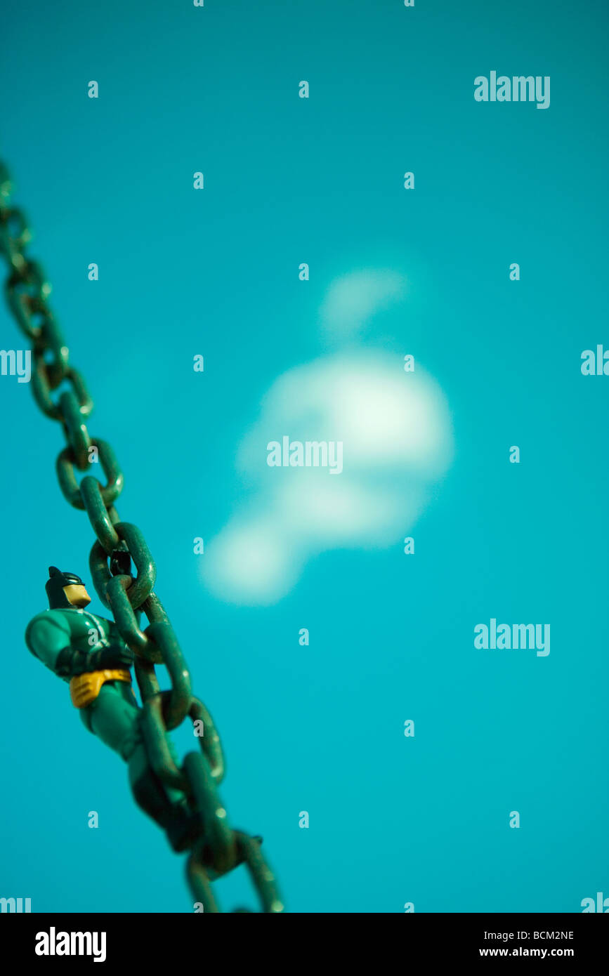 Toy figure climbing chain, blue sky and cloud in background Stock Photo