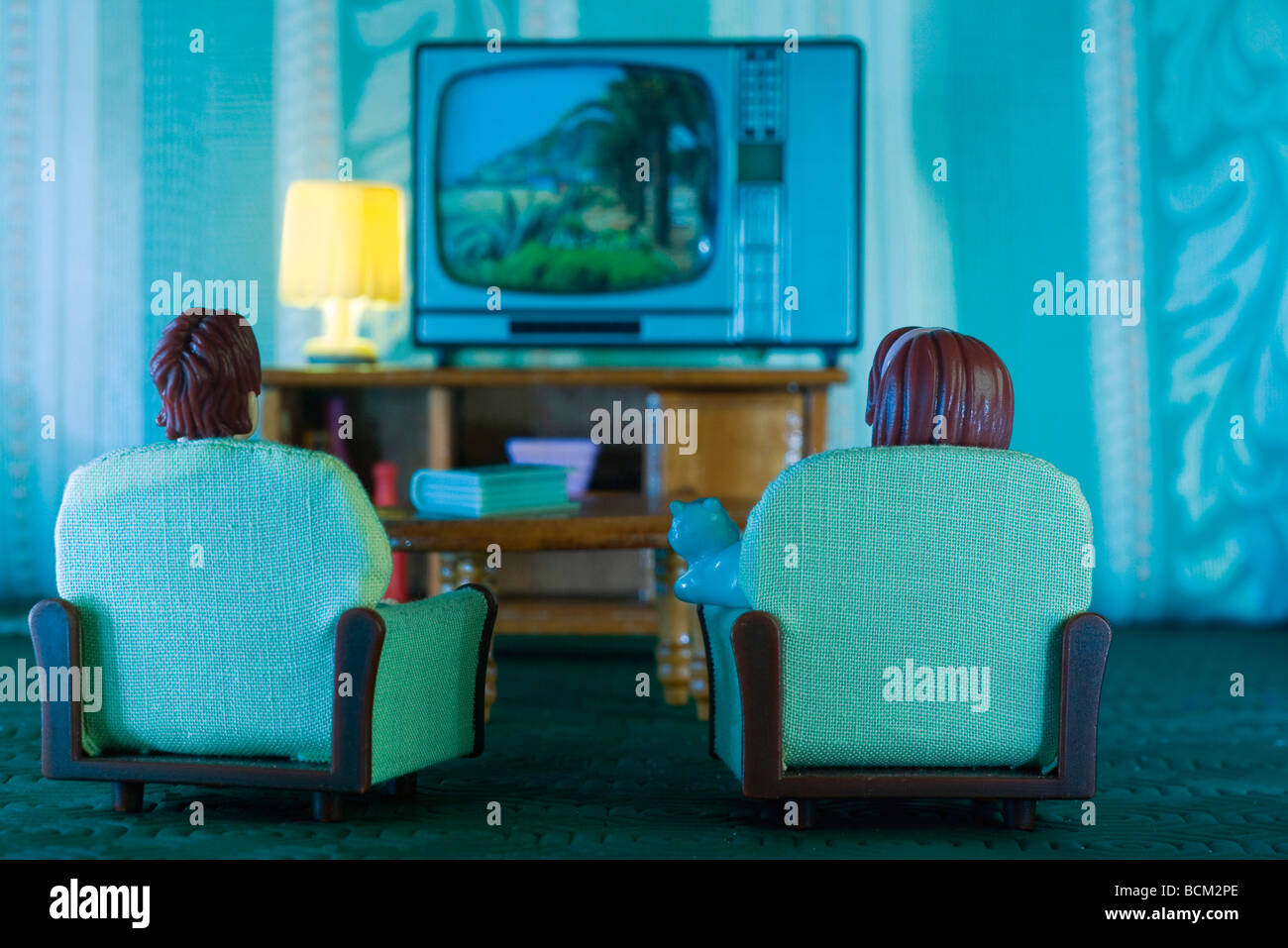 Plastic dolls sitting in armchairs, watching TV, rear view Stock Photo