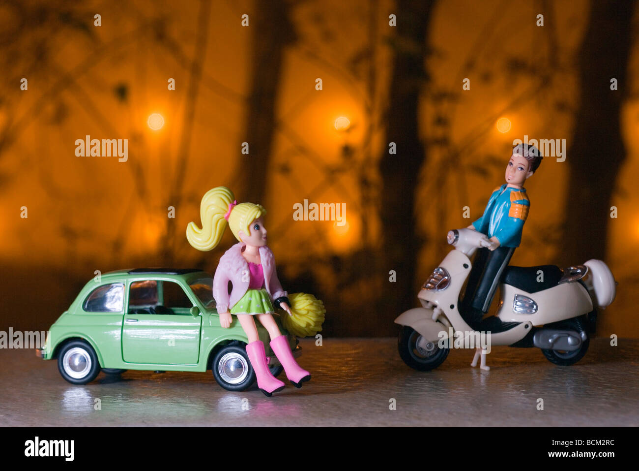 Male toy figure on moped approaching female figure leaning against toy car Stock Photo