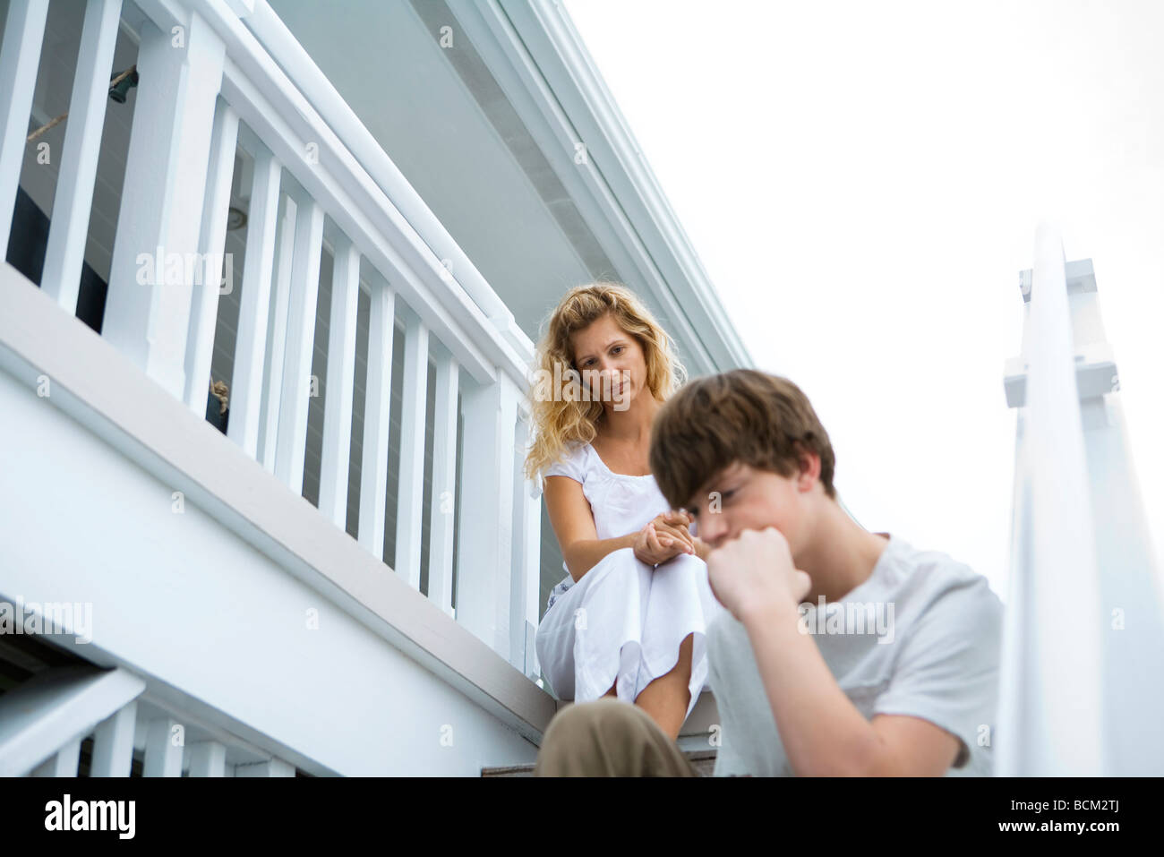 Mother and teenage son sitting on steps, son sulking Stock Photo