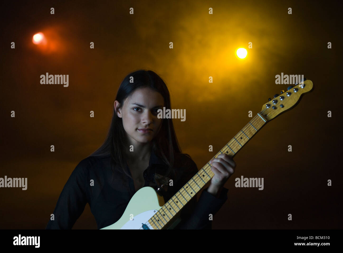 Female playing electric guitar in night club, looking at camera Stock Photo