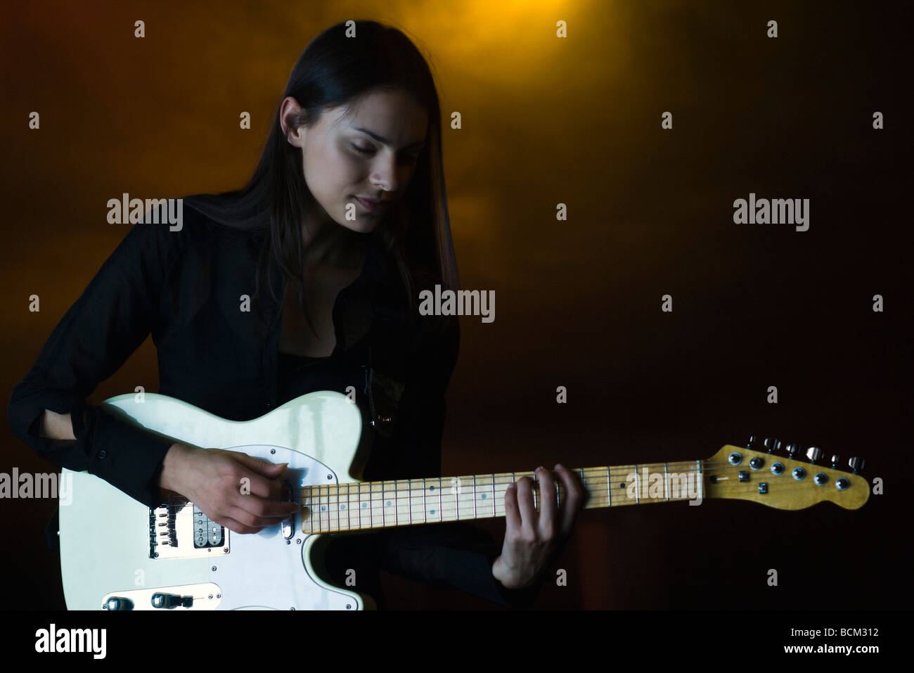 Female playing electric guitar in night club, eyes closed Stock Photo